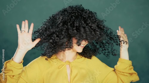 Beautiful woman with afro curly hair having fun smiling and dancing in studio against turquoise background. Music, dance concept, slow motion photo