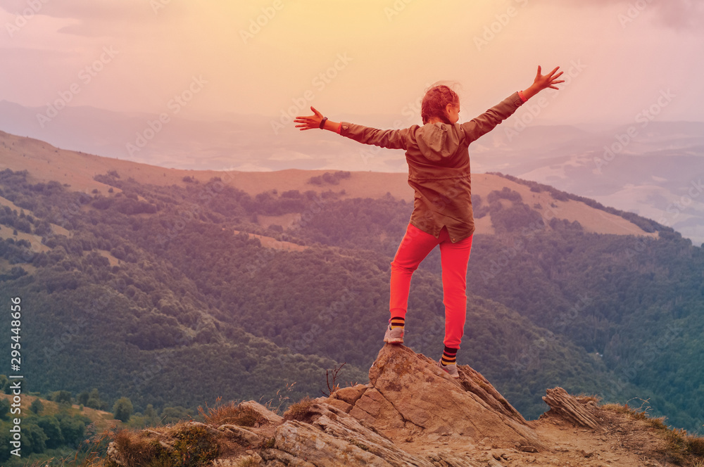 Fototapeta premium A young girl tourist stands with his hands up in happiness from on top of the mountain and enjoys a view of the Carpathian mountains at sunrise.