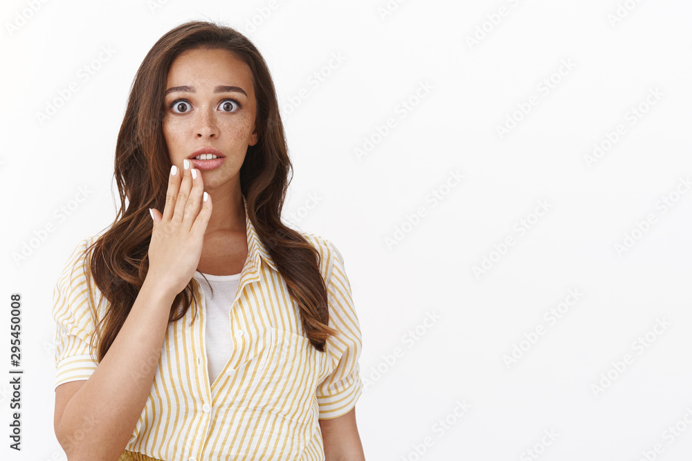 Concerned impressed young brunette woman gasping shocked, hold hand near mouth speechless and embarrassed, frowning slightly nervous, hear stunning rumor, gossiping over white background Concerned impressed young brunette woman gasping shocked, hold hand near mouth speechless and embarrassed, frowning slightly nervous, hear stunning rumor, gossiping over white background