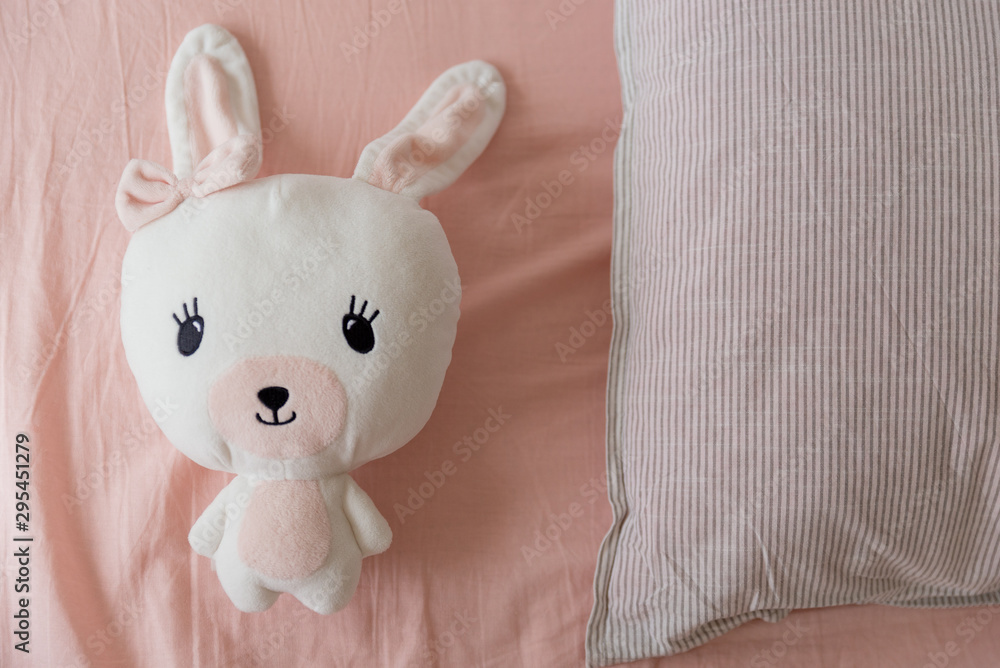 Fototapeta premium View from above on cute rabbit toy with long ears lying on pillow. Kids toy alone in bed at morning time. Concept of girlhood and children.