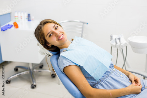 Young woman in blue jeans dress visiting the dentist and smiling sitting in dental chair.
