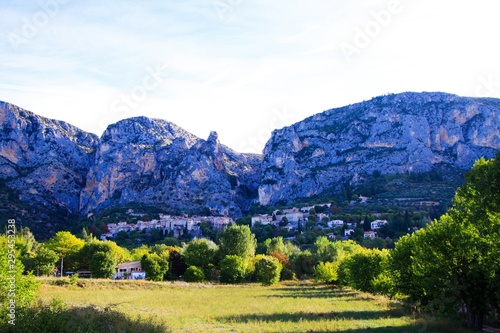 View over green valley on French village with giant mountain face background in early morning - Moustiers Sante Marie  Provence  France