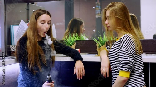 Vape lgbt teenagers. Bisexual lesbian young caucasian teenage girls smoking an electronic cigarette in vape bar. Bad habit that is harmful to health. Young pretty white caucasian teens vaping indoors.
