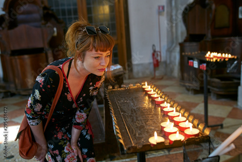 Caucasian redhead woman with floral dress looking at candles in a church in Venice photo