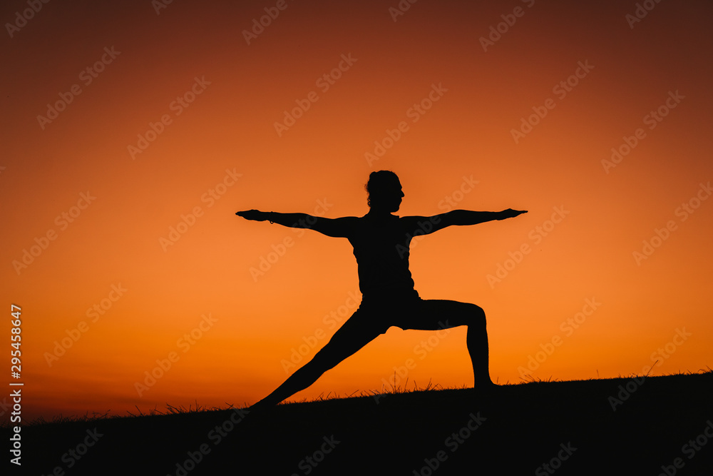 silhouette of young man in a park doing yoga sport. orange sky background. healthy lifestyle.