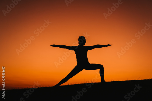 silhouette of young man in a park doing yoga sport. orange sky background. healthy lifestyle.