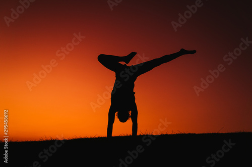 silhouette of young man in a park doing yoga sport. orange sky background. healthy lifestyle.