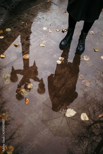 Girl in a coat, black shoes and with an umbrella. Autumn weather in the city, rain, reflection on the pavement. Drops of rain, fallen leaves.