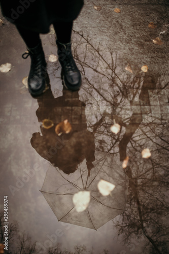 Girl in a coat, black shoes and with an umbrella. Autumn weather in the city, rain, reflection on the pavement. Drops of rain, fallen leaves.