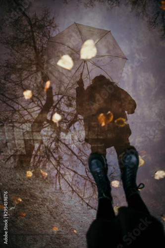 Girl in a coat, black shoes and with an umbrella. Autumn weather in the city, rain, reflection on the pavement. Drops of rain, fallen leaves.