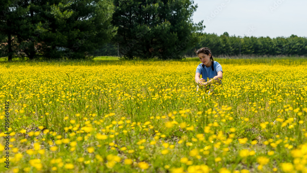 Teen girl sitting in large field with yellow flowers and trees in the background Teen girl sitting in large field with yellow flowers and trees in the background