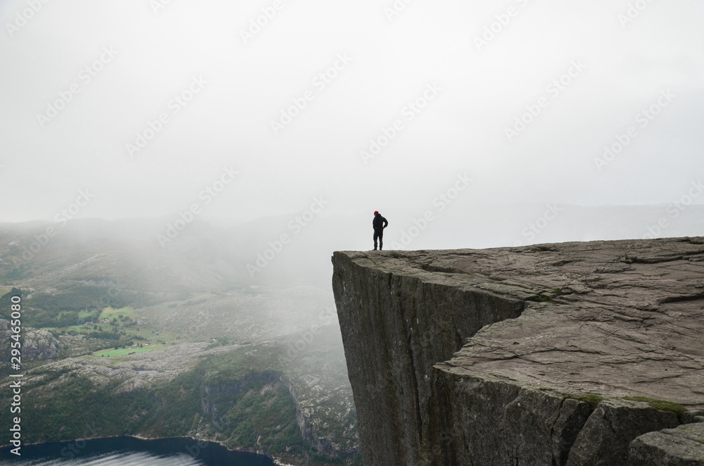 Fototapeta Mężczyzna stojący na skraju klifu Preikestolen w Norwegii. Nastrojowa letnia pogoda i piękne krajobrazy.