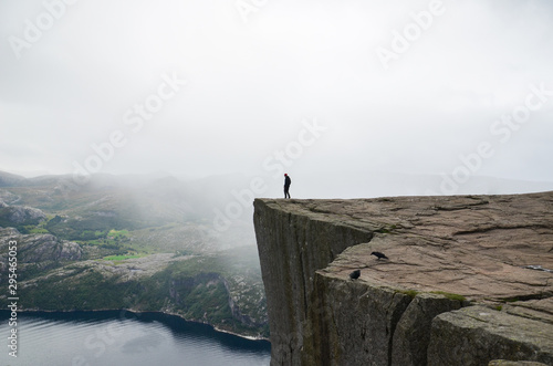 Fotografie, Obraz A man standing on the edge of the cliff Preikestolen in Norway