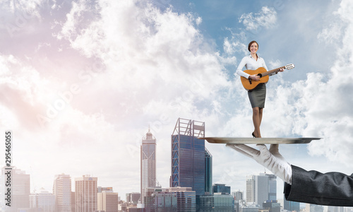 Attractive businesswoman on metal tray playing acoustic guitar against cityscape background © adam121