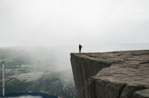 A man standing on the edge of the cliff Preikestolen in Norway. Moody summer weather and beautiful scenery. 