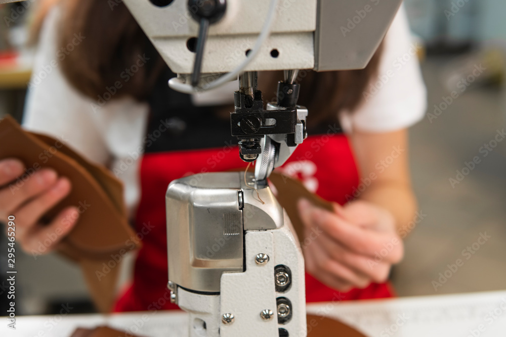 Sewing machine in a leather workshop in action with hands working on a leather details for shoes. Women's hands with sewing machine at shoes factory. Sewing machine in a leather workshop in action with hands working on a leather details for shoes. Women's hands with sewing machine at shoes factory.