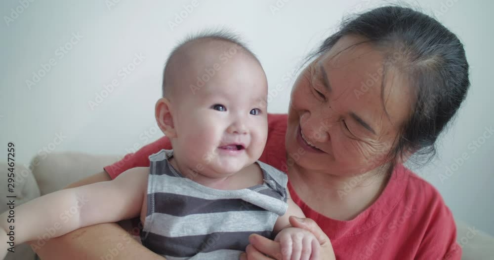 Senior asian woman holding her granddaughter baby girl at home slow motion of Chinese grandmother kissing her infant granddaughter 