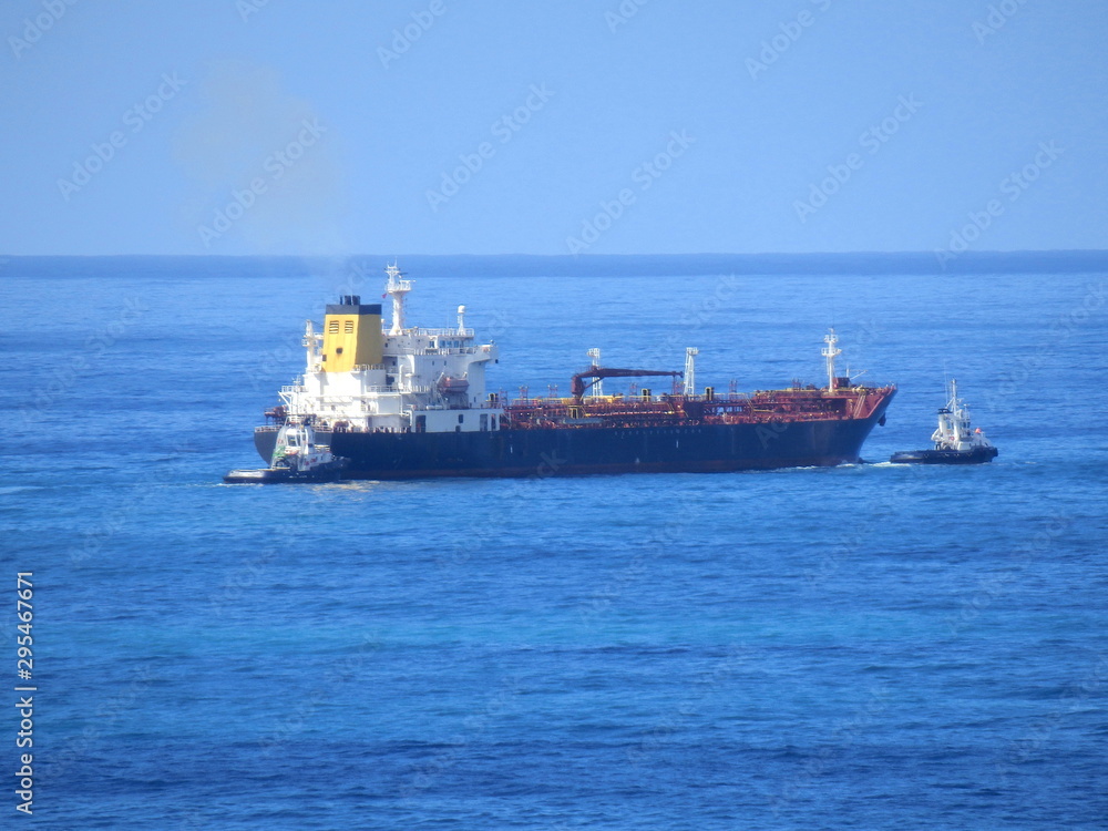 Oil tanker being escorted by two tugboats, one pushing and one pulling, sailing past the island of Madeira 
