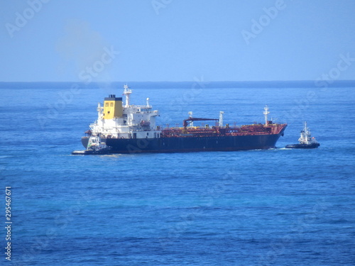 Oil tanker being escorted by two tugboats, one pushing and one pulling, sailing past the island of Madeira 