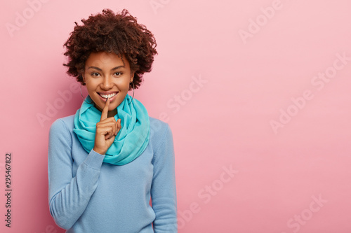 Fotografie, Obraz Indoor shot of pretty dark skinned woman asks keep quiet, makes shush gesture, g