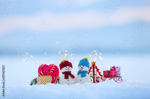 Friends snowman stay with sledge and gift box on the snow enlightened by fairy lights. Red white heart candies. Happy new year. Christmas composition.