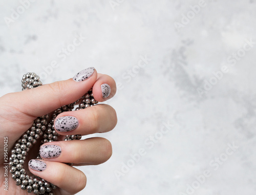 Young adult woman's hands with pink nude fashionable nails on gray concrete background