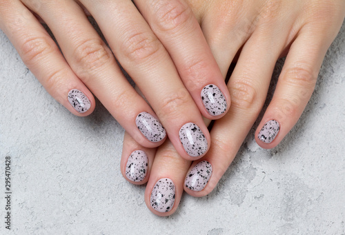 Young adult woman s hands with pink nude fashionable nails on gray concrete background
