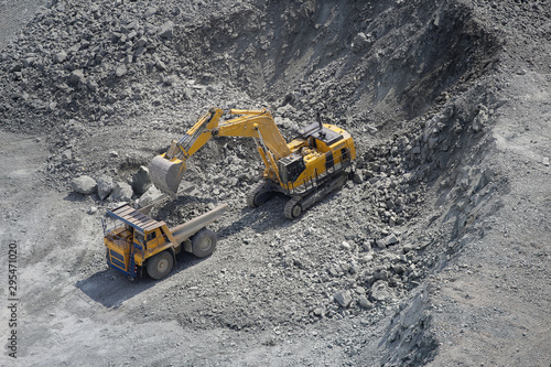 Excavator loads ore into a large mining dump truck. Open pit. Top view