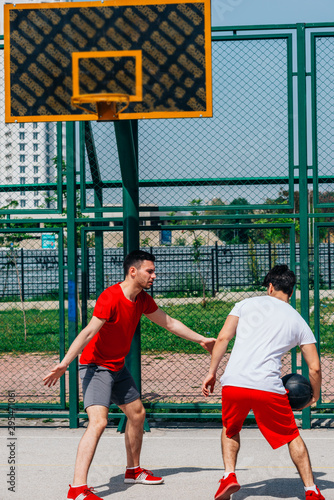 Basketball players playing ball(pushing, dribbling) on an urban basketball ground while the white skyscrapers nearly touch the blue sky.