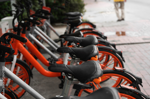 Street transportation orange hybrid rent bicycles with electronic form of payment for traveling around the city stand in row on rental network parking lot waiting for cyclists to make bike trip.