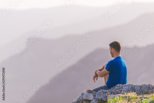 Adventurous man sitting on top of a mountain and enjoying the beautiful view  while looking downhill at the blue river and amazing mountain line..