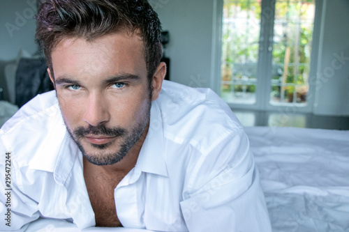 Portrait of handsome man with blue eyes and beard looking at camera with patio doors and garden in background