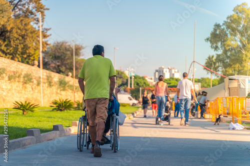 Man moving a person in a wheelchair. Taking care of a disabled person. A walk in a park with a elderly parent.