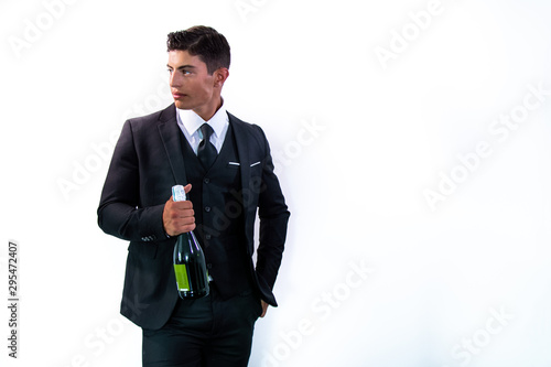 Fotografie Good looking man in suit holding bottle of sparkling wine in front of white wall