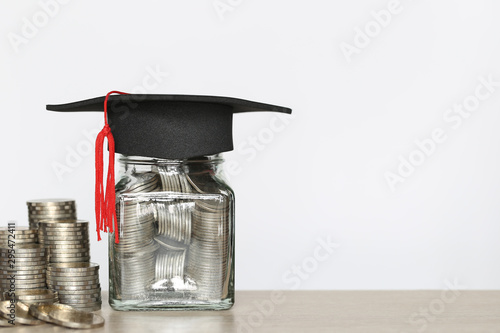 Graduation hat on the glass bottle with Stack of coins money on wtite background, Saving money for education concept photo