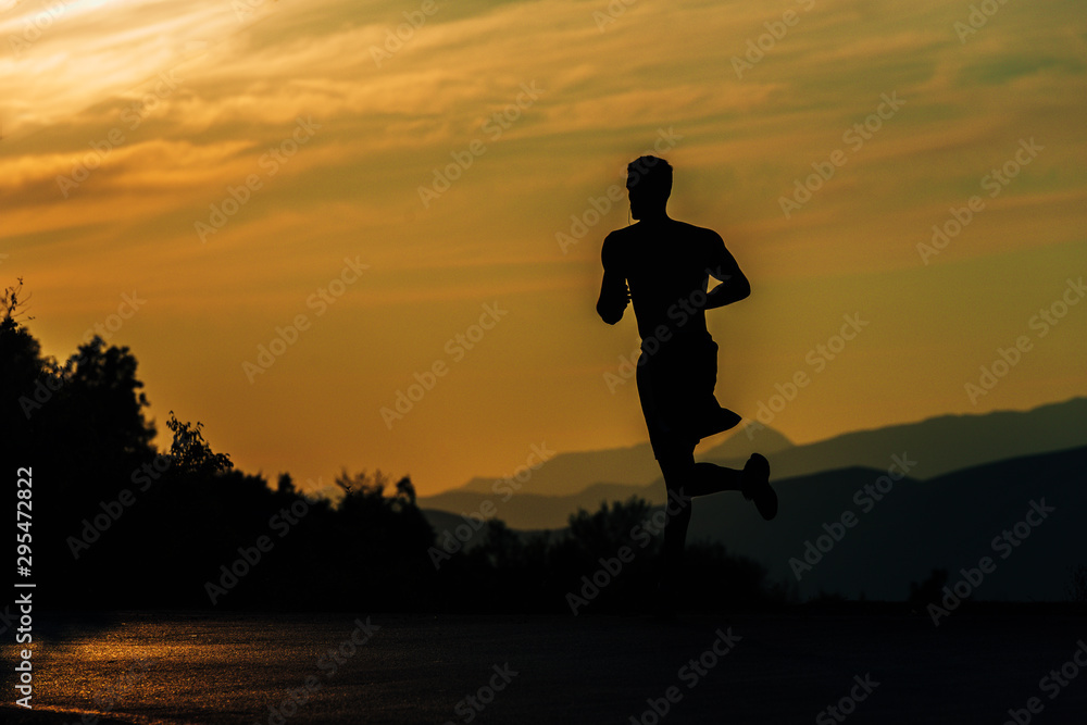 Young silhouette man exercise running outdoors keeping fit at mountain road on sunset