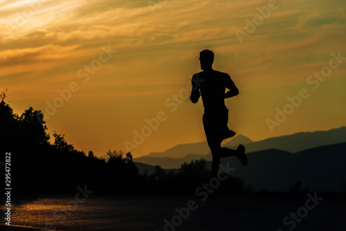 Fototapeta Naklejka Na Ścianę i Meble -  Young silhouette man exercise running outdoors keeping fit at mountain road on sunset