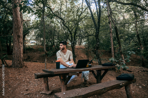 Portrait of man with laptop looking away while work in forest