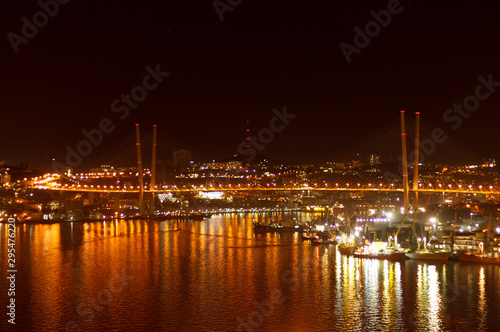 The bridge over the Golden Horn in Vladivostok and the lights of the night city reflected in the water.