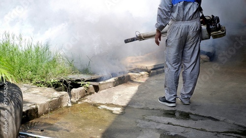 Cropped image of health personnal worker using fogging machine spraying chemical to eliminate mosquitoes and prevent dengue fever on overgrown at slum area  photo