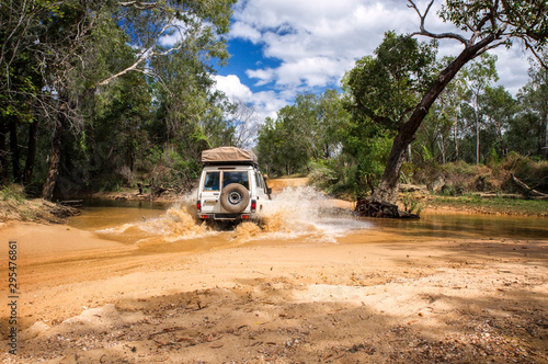 Western Australia – Flooded Outback gravel road with 4WD car crossing the waterhole with splashing muddy water at the savanna © HLPhoto