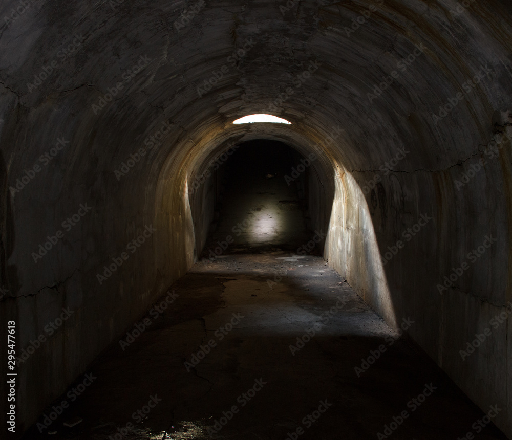 An underground corridor extending into the distance, lit through a hatch in the ceiling.