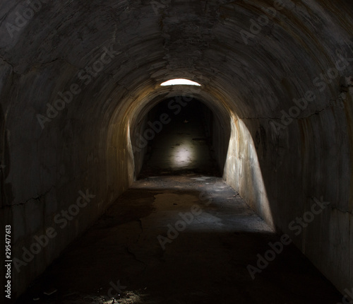 An underground corridor extending into the distance, lit through a hatch in the ceiling.