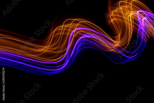 Long exposure photograph of neon gold and purple colour in an abstract swirl, parallel lines pattern against a black background. Light painting photography.