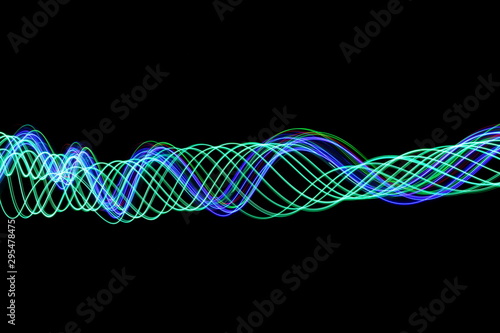 Long exposure photograph of neon green and blue colour in an abstract swirl, parallel lines pattern against a black background. Light painting photography.