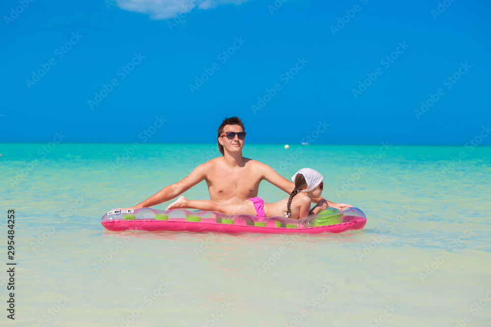 Young father with cute daughter on an air mattress in the sea