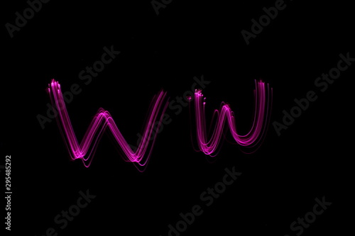 Long exposure photograph of the letter w in pink neon color, in upper case and lower case, parallel lines pattern against a black background. Light painting photography.