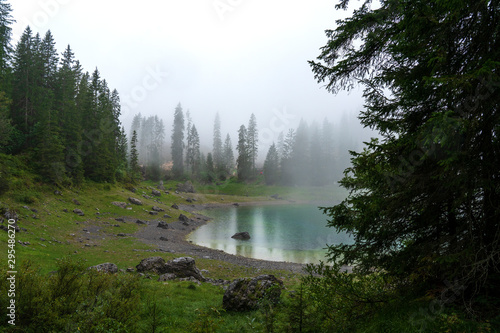 Picturesque peaks of Dolomites mountains in reflection of crystal clear pond surrounded by coniferous forest. Lake of Caresse in Italy. Scenic place and famous touristic destination. Primeval nature