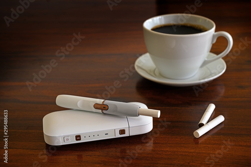 Heating tobacco system and a cup of coffee on a brown table, e-cigarette with tobacco sticks that generates a nicotine aerosol with fewer toxicants, copy space, selected focus, narrow depth of field photo