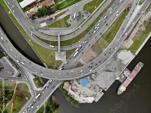 road junction near river with big cargo ship with overpass and bridge. industrial area with construction site. Aerial urban  view from top down. High traffic